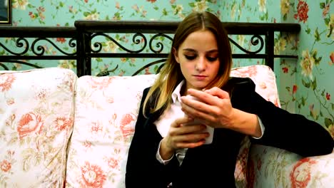 The-girl-in-a-white-shirt-and-jacket-holding-the-phone-and-looking-for-something-on-the-Internet