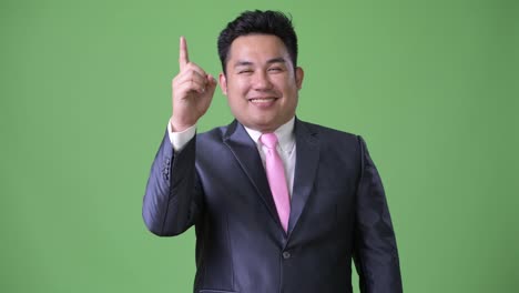 Young-handsome-overweight-Asian-businessman-against-green-background