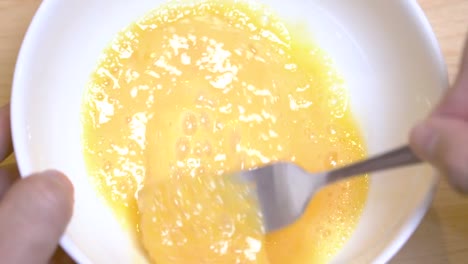 Close-up-of-hands-beat-egg-in-a-white-bowl-to-prepare-omelet-in-morning-for-breakfast.