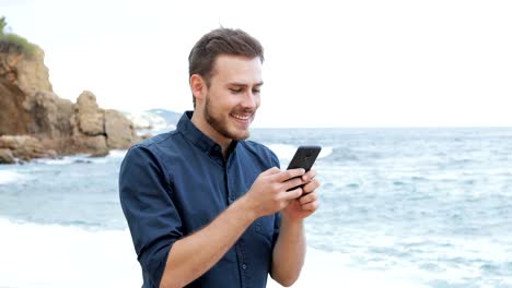 Mensajes-de-texto-del-hombre-en-teléfono-caminando-por-la-playa