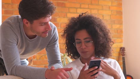 Mixed-race-couple-using-mobile-phone-in-living-room-at-home