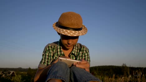 tableta-de-uso-muchacho-sentado-en-el-campo-al-atardecer,-al-aire-libre