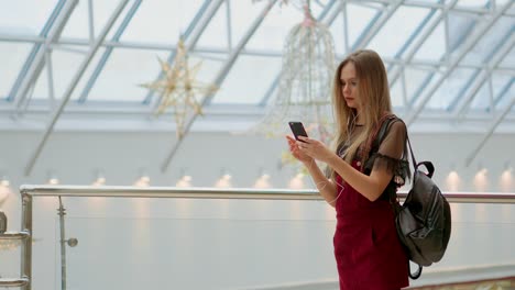 Girl-with-a-backpack-talking-on-video-coll-through-headphones-and-a-mobile-phone-at-the-airport.-posing-for-selfie-on-smartphone-camera,-hipster-girl-enjoying-radio-broadcast-making-photo-for-picture-in-social-networks-on-mobile