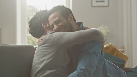 Pareja-Gay-hombre-dulce-completo-alrededor-en-un-sofá-en-casa.-Novio-corre-y-salta-en-manos-de-su-pareja.-Abrazan.-Ellos-son-feliz-y-ríe.-Son-vestidos-casualmente-y-sala-tiene-un-Interior-moderno.