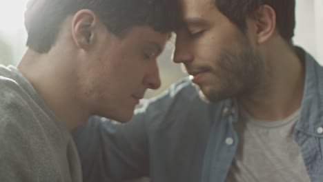 Cerca-de-una-linda-pareja-gay-hombre-tomados-de-la-mano-y-juntando-sus-cabezas-y-cerrar-los-ojos.-Suave-dulce-amor-momento-de-relación-Gay.-Habitación-tiene-un-Interior-moderno.