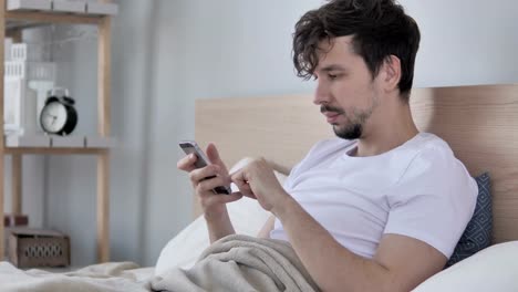 Mann-mittels-Smartphone-beim-liegen-auf-der-Seite-im-Bett