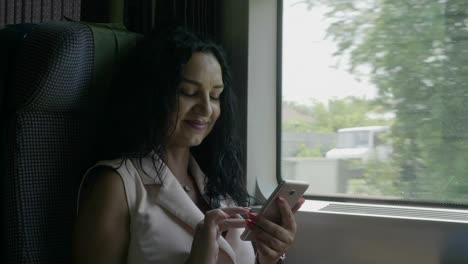 Mujer-joven-con-estilo-conmutando-en-el-tren-sonriendo-mientras-navega-por-Internet-navegando-en-redes-sociales-en-el-teléfono-inteligente