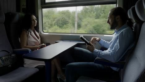 Young-business-man-commuting-from-work-to-home-using-a-tablet-pc-talking-and-flirting-with-elegant-attractive-young-woman-during-travel