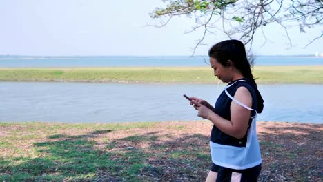 Asiatische-Mädchen-gehen,-trainieren-und-benutzen-das-Telefon-in-der-Natur-mit-der-Sonne-am-Morgen.-Konzept-Gesundheit-mit-Bewegung.-Zeitlupe