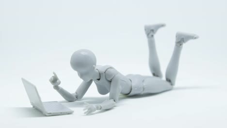 Stop-motion-footage-robot-woman-is-lying-down-and-playing-laptop-on-the-floor-with-white-background.