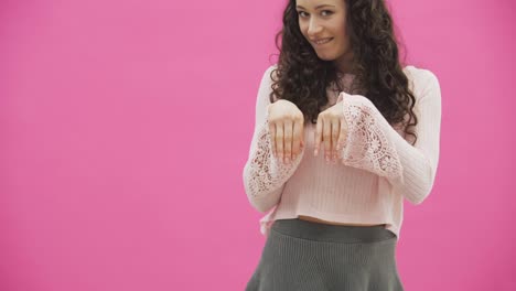 Young-beautiful-girl-standing-on-a-pink-background.-A-gray-skirt-and-a-pink-sweater-with-hooked-ears-on-the-head.-Smiling-mimics-the-movements-of-the-hounds.-Easter-concept.