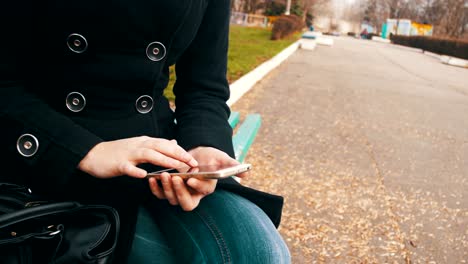 Junge-Frau-mit-Smartphone-auf-einer-Bank-im-Stadtpark