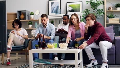 Hombres-y-mujeres-usando-teléfonos-inteligentes-y-luego-viendo-noticias-en-la-televisión-juntos-en-casa