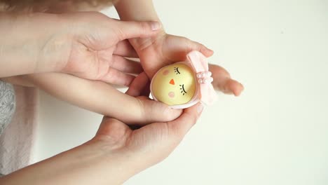 Women's-and-children's-hands-hold-chicken-egg-decorated-for-Easter-chick-with-painted-face.