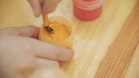 Creative-boy-is-mixing-and-stirring-yellow-paint-in-a-jar-with-a-help-of-nude-paint-brush.