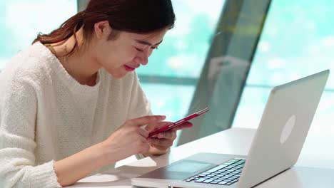 pretty-young-asian-woman-using-mobile-phone-and-laptop-indoor