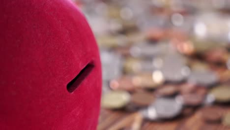 Close-up-for-moneybox-with-coins-falling-on-the-old-wooden-table,-saving-money-concept.-Pink-moneybox-with-many-coins-falling-and-lying-on-the-table.