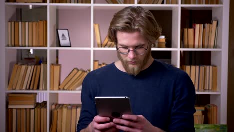 Sesión-de-primer-plano-de-adulto-estudiante-masculino-atractivo-usando-la-tableta-en-la-biblioteca-de-la-universidad-en-el-interior