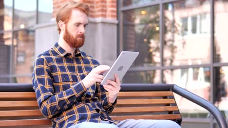 Rotschopf-Bart-junge-Mann-mit-Tablet,-während-auf-der-Bank-sitzen