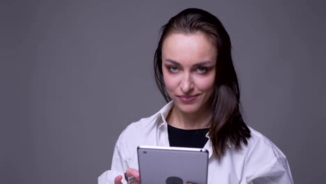 Nahaufnahme-Porträt-von-erwachsenen-attraktiven-kaukasischen-Frau-mit-dem-Tablet-und-lächelnd-Blick-auf-die-Kamera-mit-Hintergrund-isoliert-auf-grau