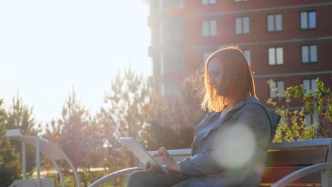 Woman-using-tablet-computer-sitting-on-bench-in-city