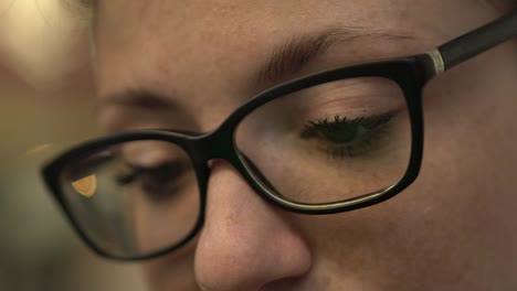 Close-up-of-eyes-of-attractive-cool-redhead-woman-with-glasses-reflection,-freckles-and-red-hair-watching-internet-video-on-smartphone-sitting-at-bus-stop-in-street,-during-sunny-summer-in-Paris.