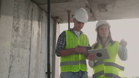 Engineers-designers-stand-on-the-roof-of-the-building-under-construction-and-discuss-the-plan-and-the-progress-of-construction-using-a-tablet-and-mobile-phone