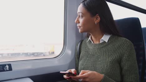 Businesswoman-Sitting-In-Train-Commuting-To-Work-Checking-Messages-On-Mobile-Phone