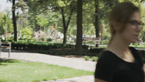 Pretty-young-caucasian-woman-in-eyeglasses-walking-towards-camera,-checking-phone-and-celebrating-good-news-in-a-park