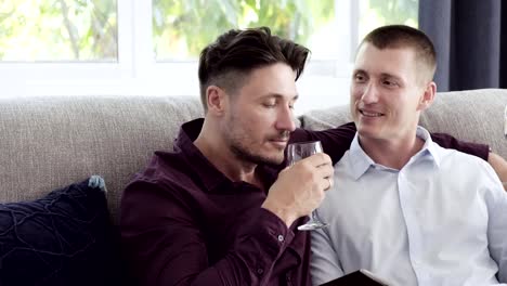 Pareja-gay-relajándose-en-el-sofá.-Beban-vino-juntos.