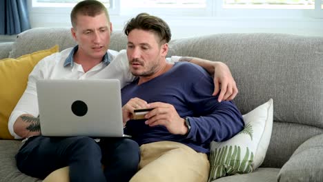 Gay-couple-relaxing-on-couch-using-laptop-computer.-Keying-in-credit-card-number.