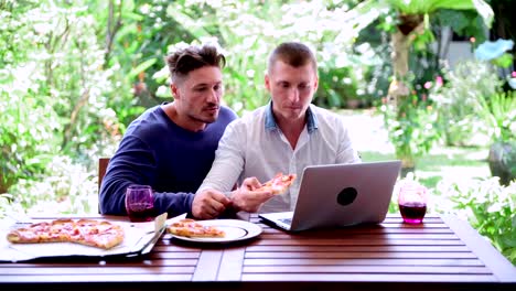 Gay-couple-having-pizza-for-lunch.-Biting-pizza,-talking.