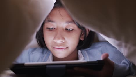 Asian-Little-girl-using-tablet-under-blanket-in-the-bedroom-at-night