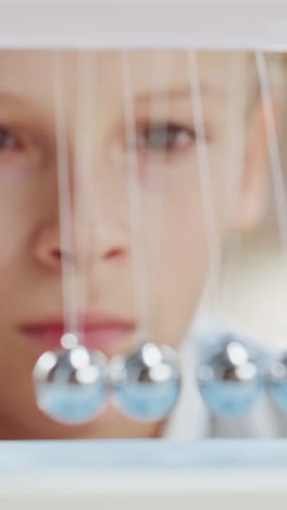 Retrato-de-cerca-de-un-joven-curioso-mirando-a-newton's-Cradle.-Aprendizaje-Infantil-sobre-Física.-Video-De-archivo-con-orientación-vertical-de-la-pantalla-9:16