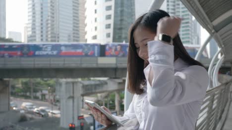 Side-view-of-Excited-business-asian-woman-celebrating-good-news-checking-smart-phone-in-the-modern-city-center-of-Bangkok-Thailand.-Concept-Technology-communication,-success-by-mobile-phone