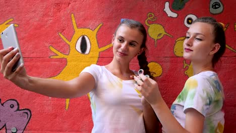 Selphi-of-girls-with-spinners-in-arms-on-background-of-graffiti,-Girlfriends-make-photo-on-phone-with-toy-for-stress-relief