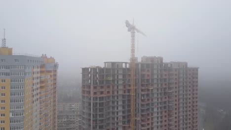 Aerial-view.-A-multi-storey-brick-house-in-the-city-in-a-fog.-A-construction-crane-is-installed-on-the-site-of-the-construction-of-a-residential-building.-New-homes-for-sale-and-rent-of-real-estate