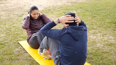 Al-aire-libre-del-entrenamiento-de-pareja.-Pareja-joven-de-América-Latina-sientan-ups-en-común-amarillo-mat-en-el-Parque-otoño-lluvioso-como-parte-del-programa-habitual-de-ejercicios.