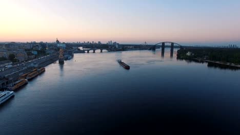 Barge-sails-along-the-river-near-the-city-port-on-sunset-aerial-footage