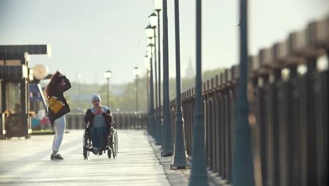 Hombre-discapacitado-en-silla-de-ruedas-toma-imágenes-de-la-joven-en-el-muelle