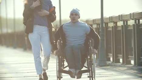 Young-disabled-man-in-a-wheelchair-walking-with-young-woman-on-the-quay-and-talking