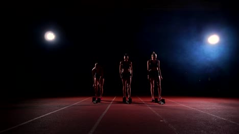 Corredores-femeninos-en-atletismo-pista-agachado-en-los-bloques-de-salida-antes-de-una-carrera.-En-cámara-lenta