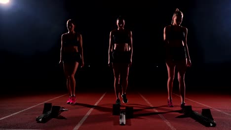 Corredores-femeninos-en-atletismo-pista-agachado-en-los-bloques-de-salida-antes-de-una-carrera.-En-cámara-lenta