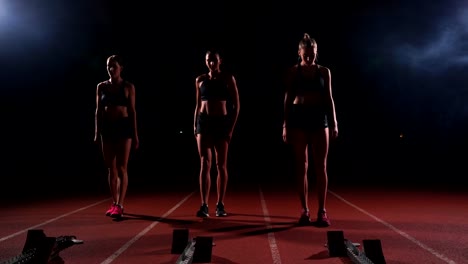 Corredores-femeninos-en-atletismo-pista-agachado-en-los-bloques-de-salida-antes-de-una-carrera.-En-cámara-lenta