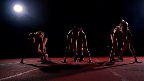 Female-runners-at-athletics-track-crouching-at-the-starting-blocks-before-a-race.-In-slow-motion