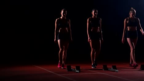 Corredores-femeninos-en-atletismo-pista-agachado-en-los-bloques-de-salida-antes-de-una-carrera.-En-cámara-lenta