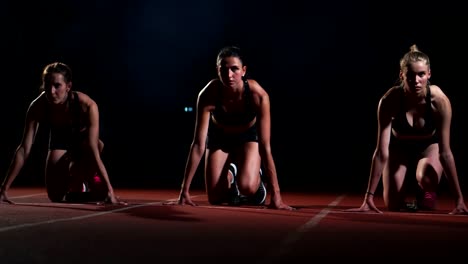 Three-sports-girl-athletes-at-night-on-the-treadmill-start-for-the-race-at-the-sprint-distance-from-the-sitting-position