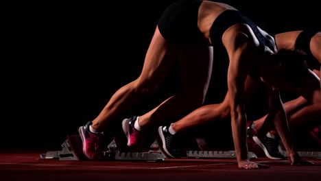 Tres-chicas-en-ropa-de-color-negro-están-en-las-almohadillas-de-partida-para-iniciar-la-carrera-en-la-competencia-a-la-luz-de-las-linternas