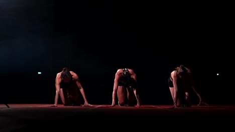 Tres-chicas-en-ropa-de-color-negro-están-en-las-almohadillas-de-partida-para-iniciar-la-carrera-en-la-competencia