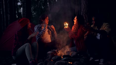 Creative-people-are-congratulating-their-friend-on-birthday-in-forest,-clapping-hands-and-giving-her-cake-while-girl-is-blowing-candles-and-smiling.-Nature-and-celebration-concept.